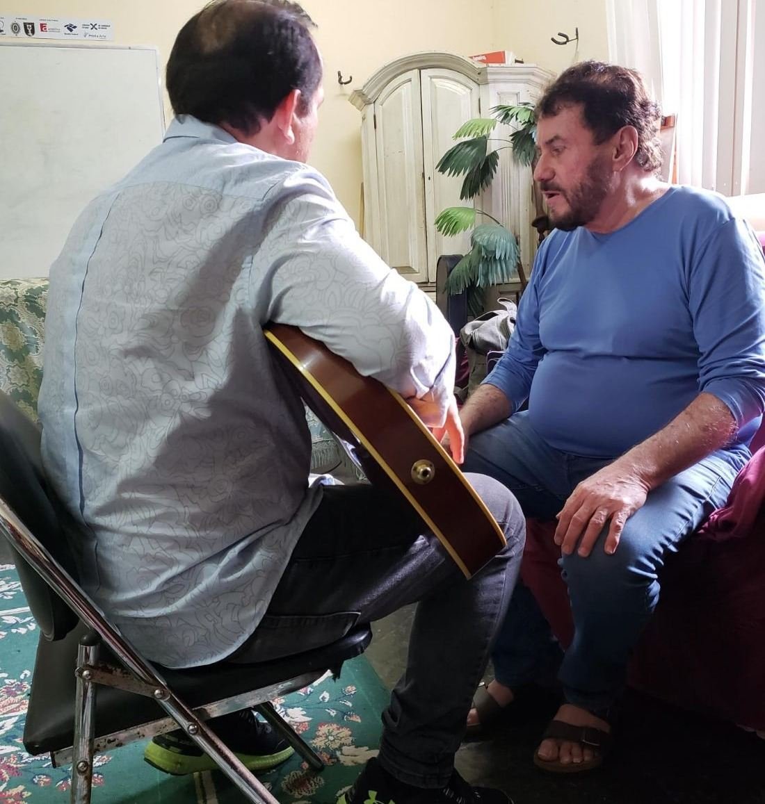 Um cantor e violonista ensinando acordes de violão a Edilásio Jr.