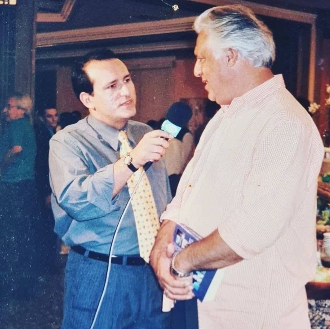 Edilásio Jr. entrevistando o ator Antônio Fagundes, que segura um livro, com o microfone verde da Band