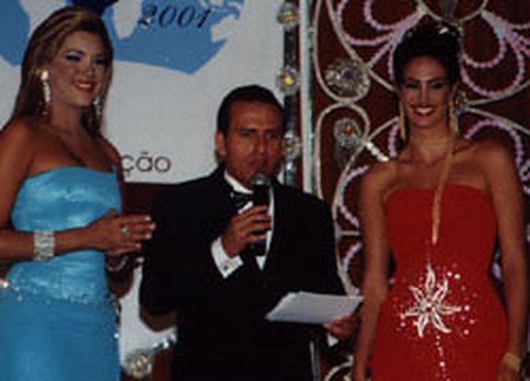 Edilásio Jr. de smoking, ao microfone, apresentando o Miss Brasil entre duas misses