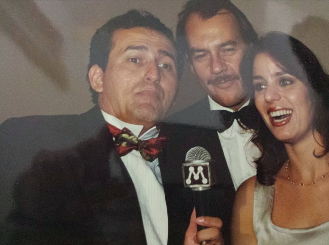 Edilásio Jr. de smoking com o ator Paulo César Grande e a atriz Cláudia Mauro, com o microfone da TV Manchete
